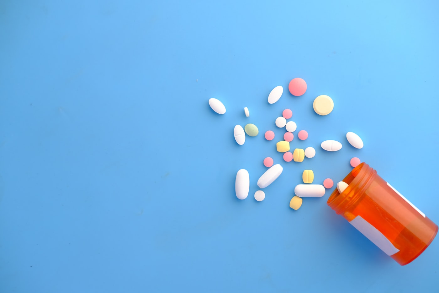 Colourful pills spilling from an orange bottle